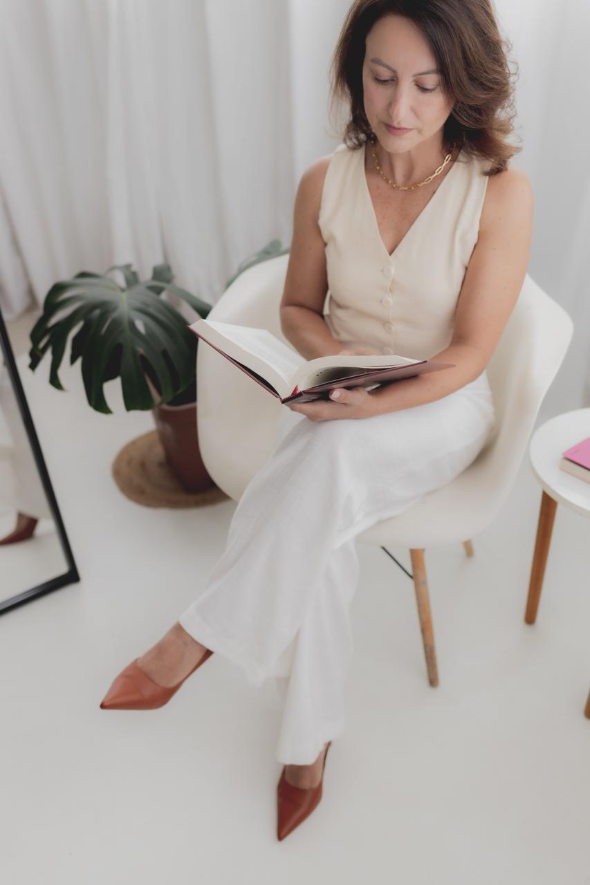 Vanessa Helena sentada com um livro em um ambiente claro e tranquilo